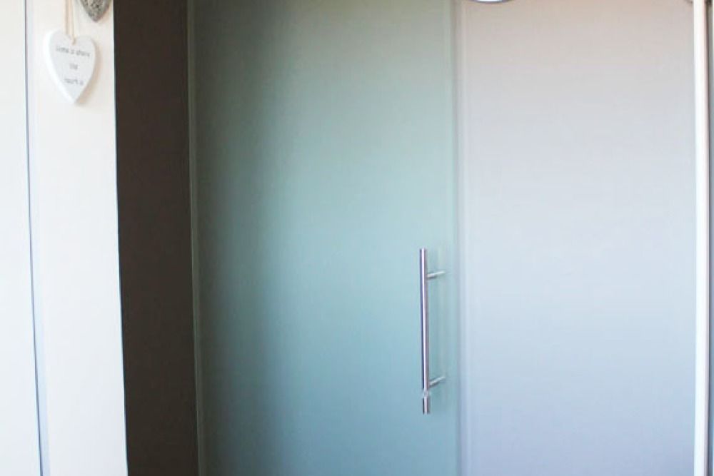 Porta scorrevole in vetro smerigliato con maniglia argentata, parete bianca adiacente e decorazione a forma di cuore.