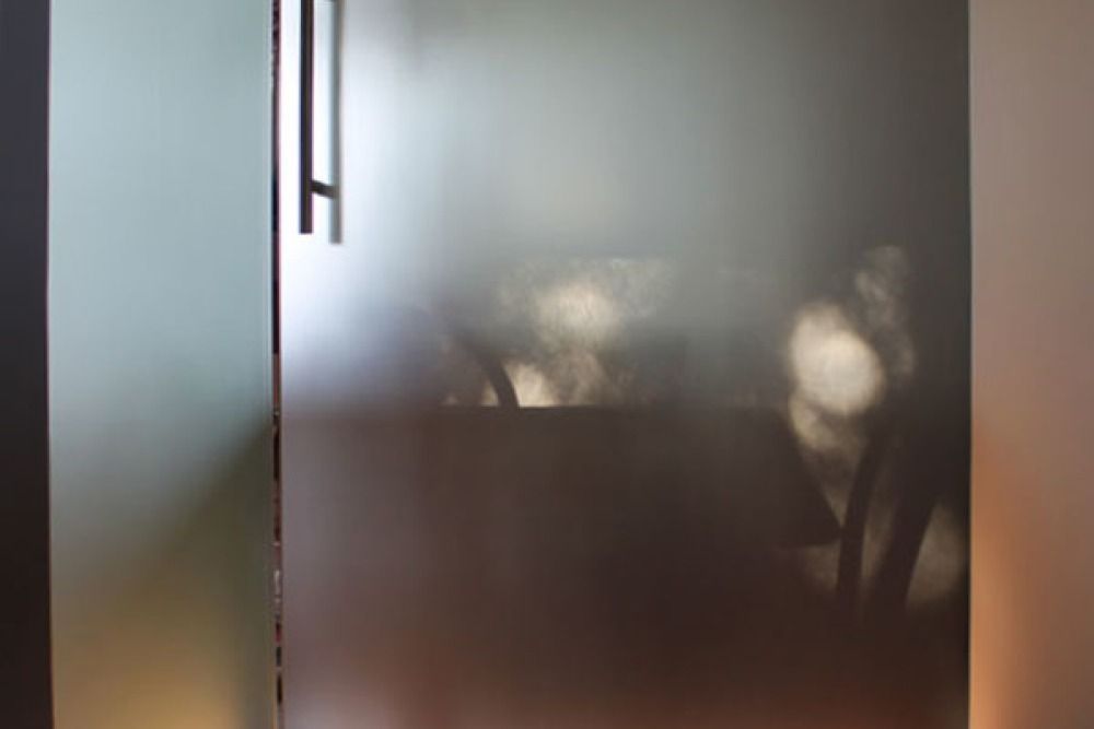 Porta in vetro smerigliato con maniglia scura; ombre proiettate all'interno.