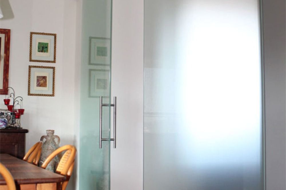 Porta in vetro smerigliato con maniglia argentata, aperta, che conduce a uno spazio più luminoso.