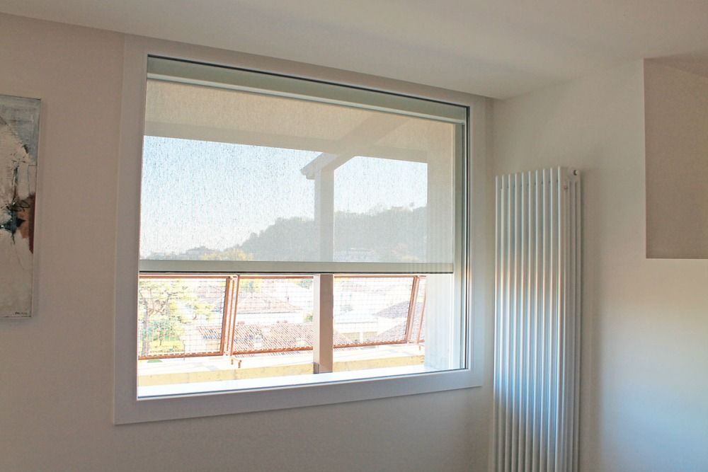 Finestra con tenda avvolgibile bianca parzialmente abbassata; sulla destra c'è un termosifone.