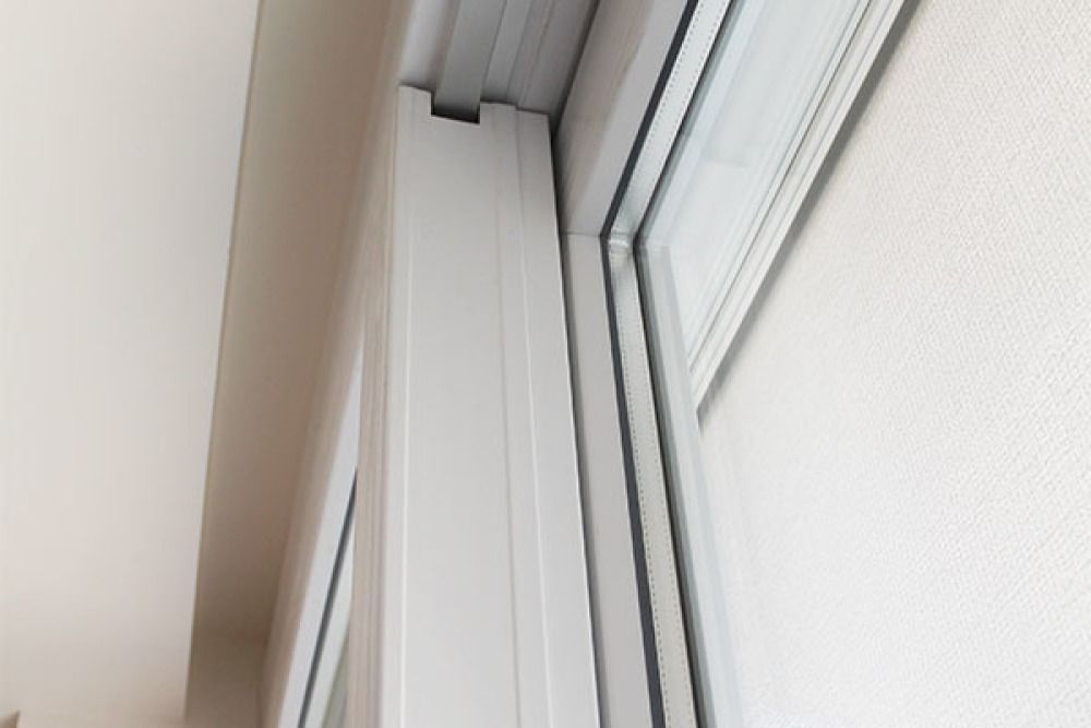 Primo piano del telaio di una finestra bianca e del muro circostante; si vede l'angolo superiore.