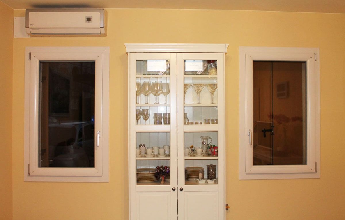 Mobiletto bianco tra due finestre e sopra un condizionatore, su una parete gialla.