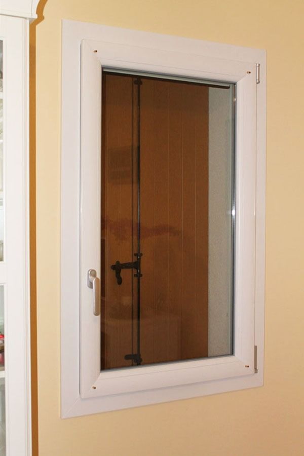 Finestra con cornice bianca su una parete gialla, il vetro riflette una porta marrone.