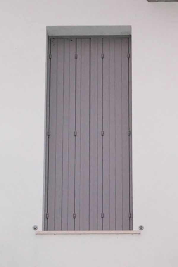 Persiane grigie che coprono una finestra di un edificio bianco.