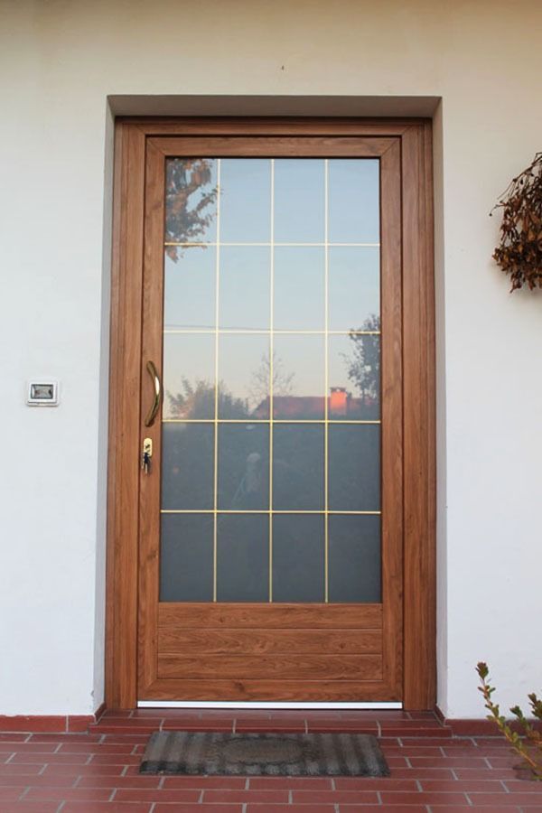 Porta d'ingresso in legno con grande pannello in vetro, portico in mattoni e parete bianca.