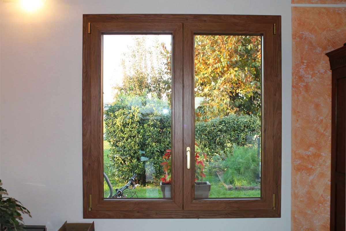 Finestra con cornice in legno che si affaccia su un rigoglioso giardino verde in una giornata di sole.