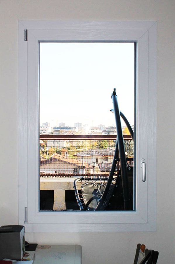 Finestra che incornicia un paesaggio urbano con una struttura metallica nera in vista; cielo luminoso sopra gli edifici.