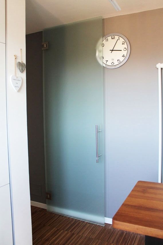 Porta in vetro smerigliato con maniglia e cerniere in una stanza con un orologio sul muro.