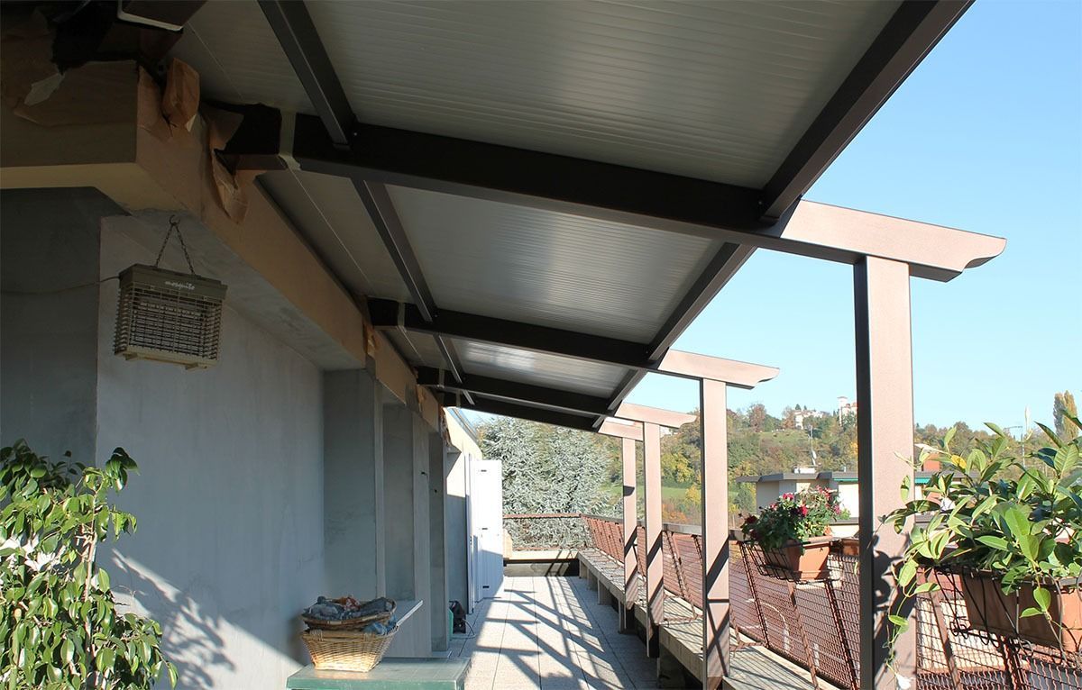 Un balcone esterno coperto con una tenda da sole in metallo e plastica, una ringhiera e piante.