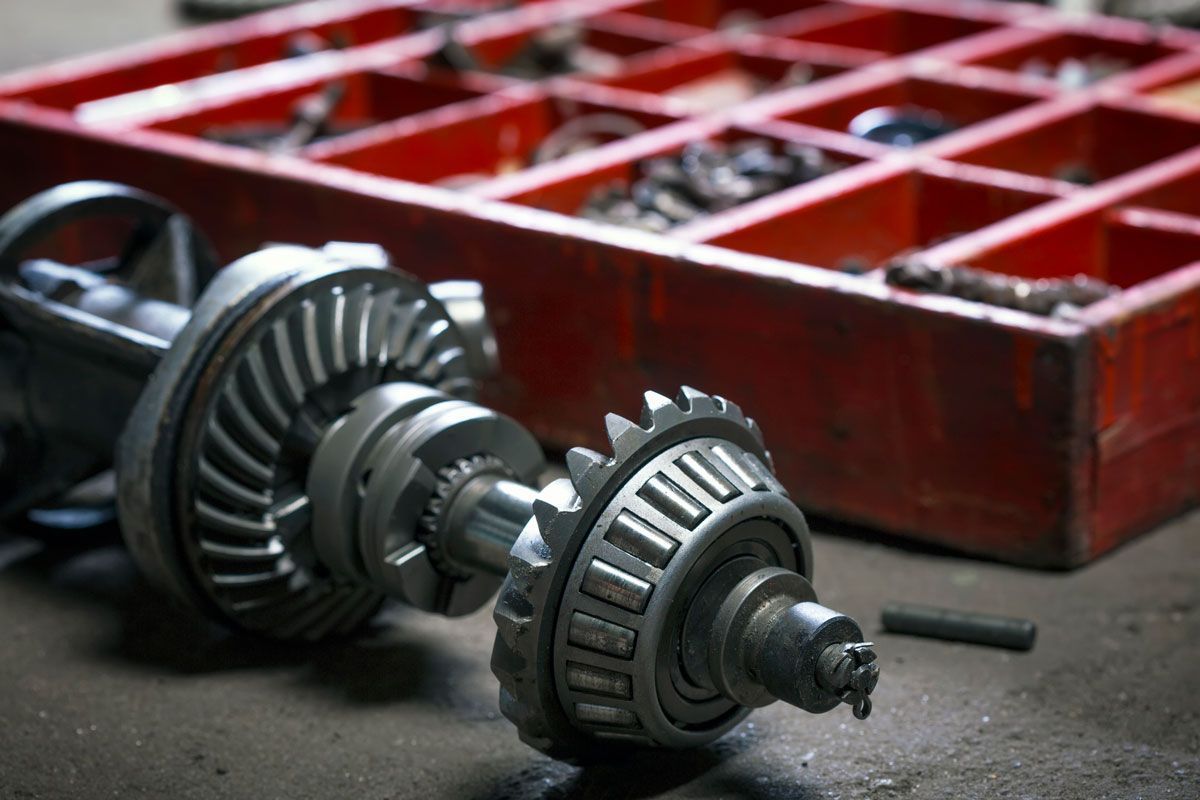 Disassembled car differential with gears, bearings, and a red parts organizer in a workshop.