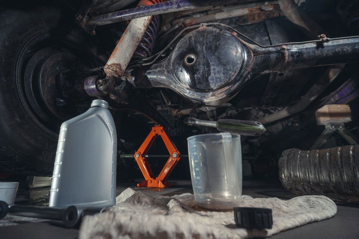 Car undercarriage, leaking oil, with tools and containers underneath.