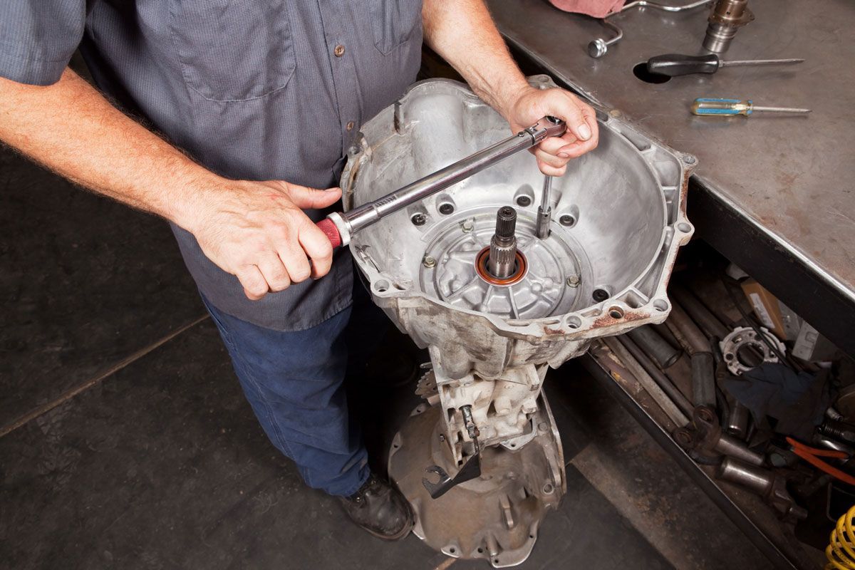 Mechanic uses a wrench on a car transmission in a repair shop.