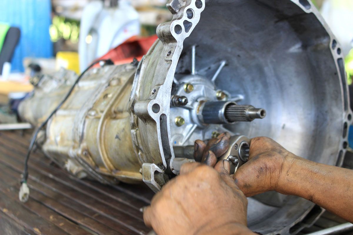 Hands repairing a car transmission with tools, focusing on the internal components.