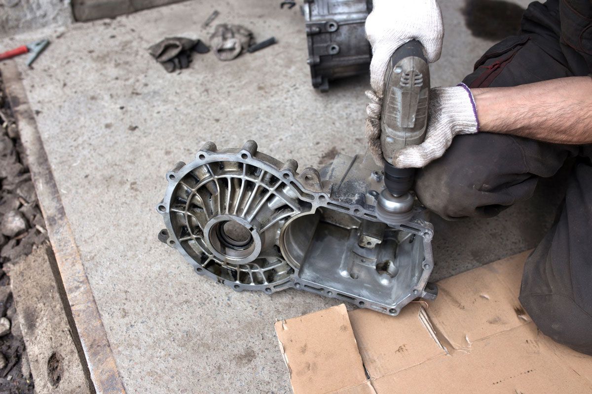 Person using a power tool on a vehicle transmission case outdoors.