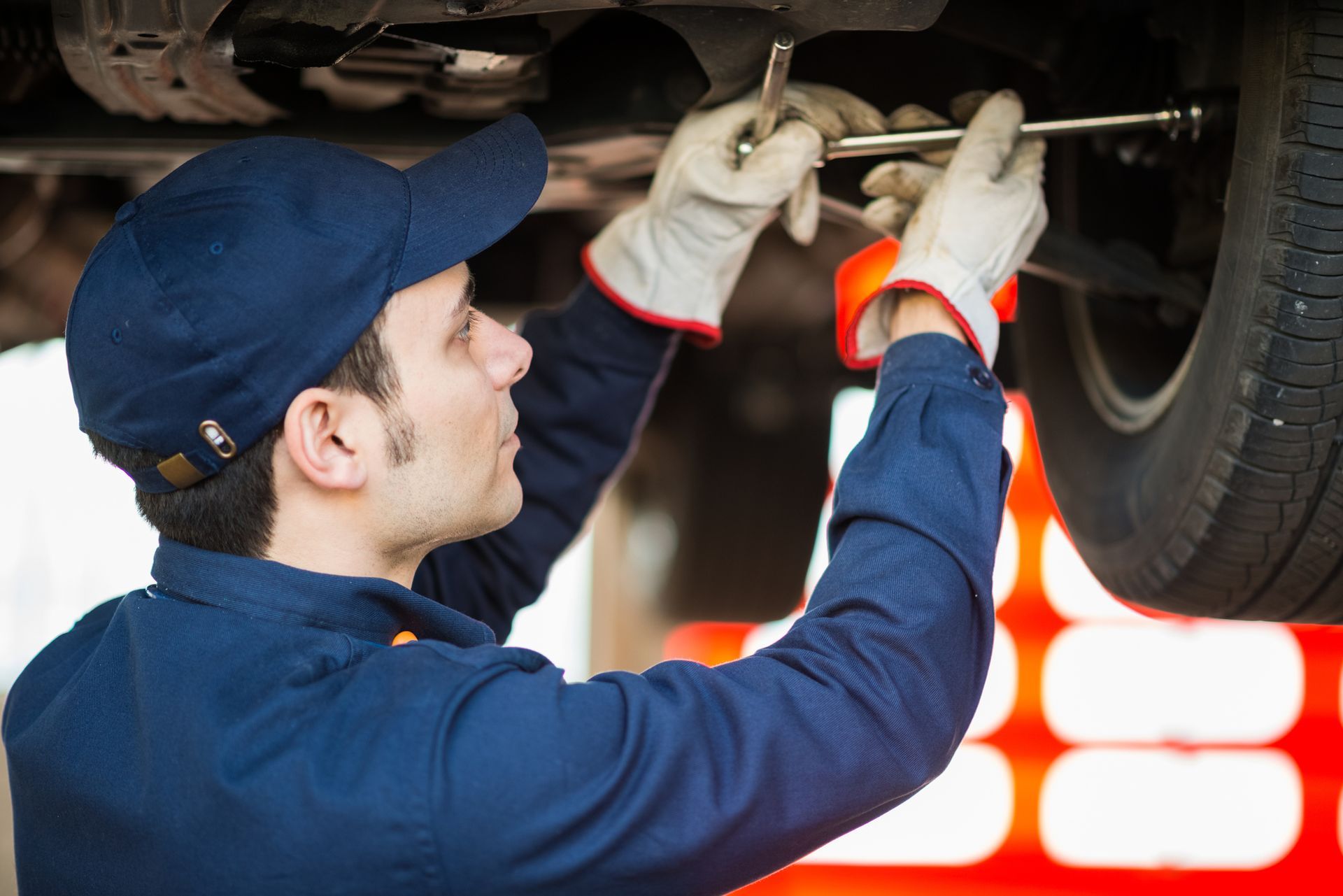 Auto technician performing undercar repair with wrench in professional vehicle service bay.