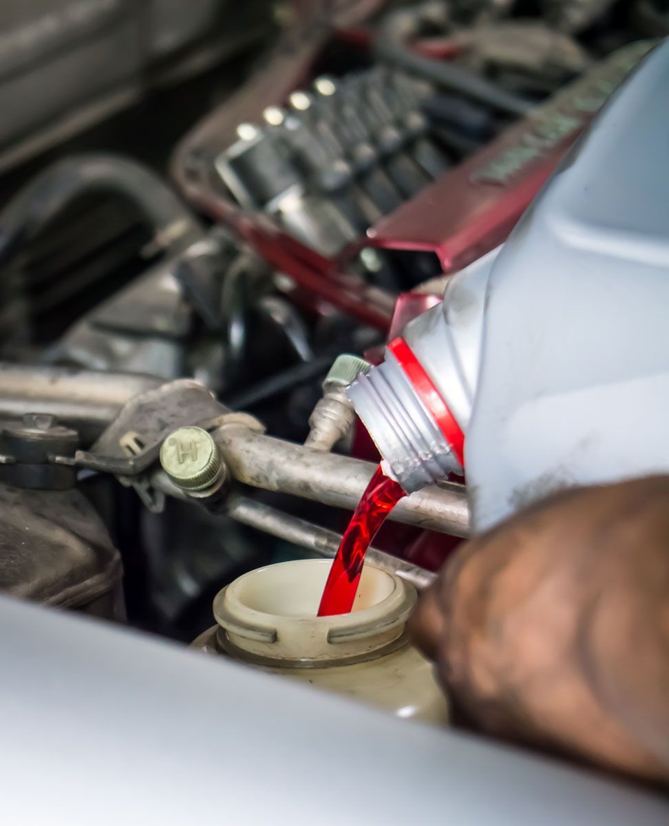 Person pouring red fluid into a car's reservoir under the hood.
