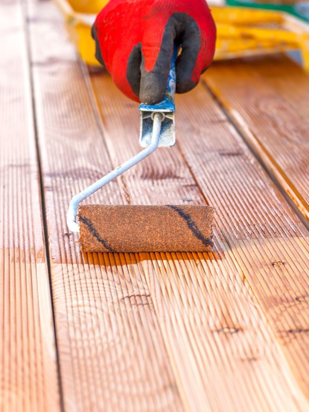 A person is painting a wooden deck with a roller.