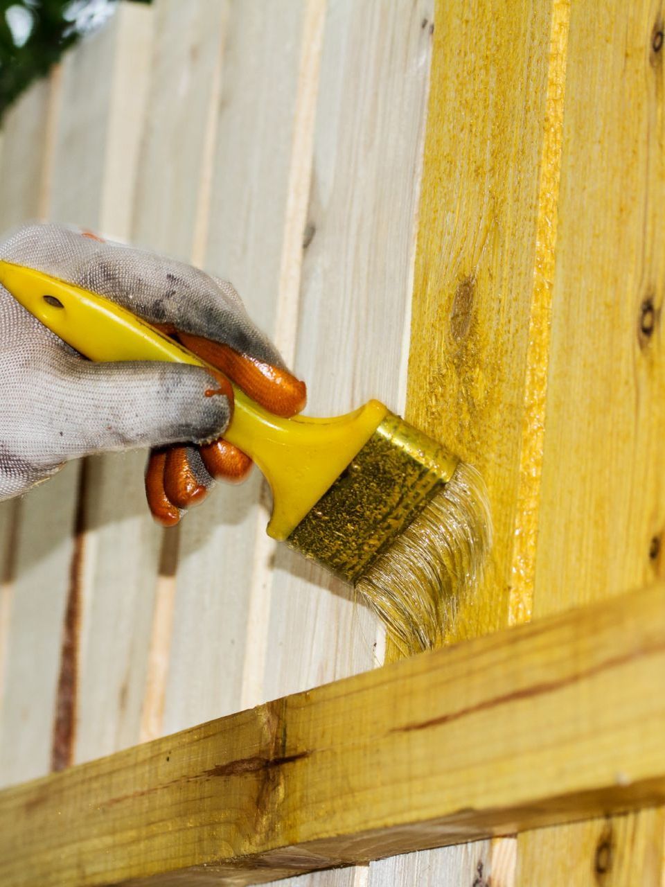 A person is painting a wooden fence with a yellow brush.