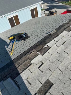 High-angle view of a grey shingled roof under construction with tools laid out, showing partially replaced shingles.