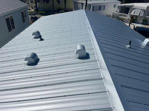 A view looking down at a metal roof with two distinct panel styles and several vent hoods in a residential neighborhood.