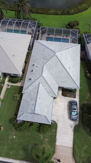 Aerial view of a residential home with a gray roof, a backyard pool with a screen enclosure, and a car in the driveway.
