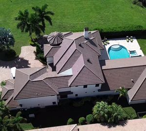 Aerial view of a large white house with a multi-gabled brown tiled roof, pool, and surrounding green lawn.