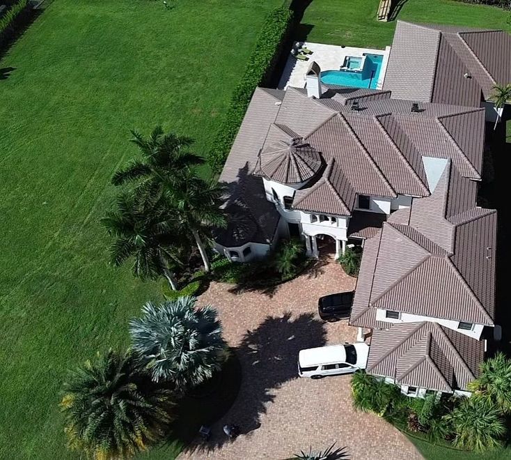 Aerial view of a large white house with a brown tile roof, a swimming pool, and a driveway with two parked vehicles.