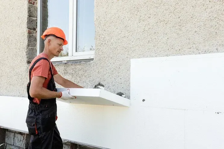 Professional installer fitting external wall insulation boards on a residential property exterior