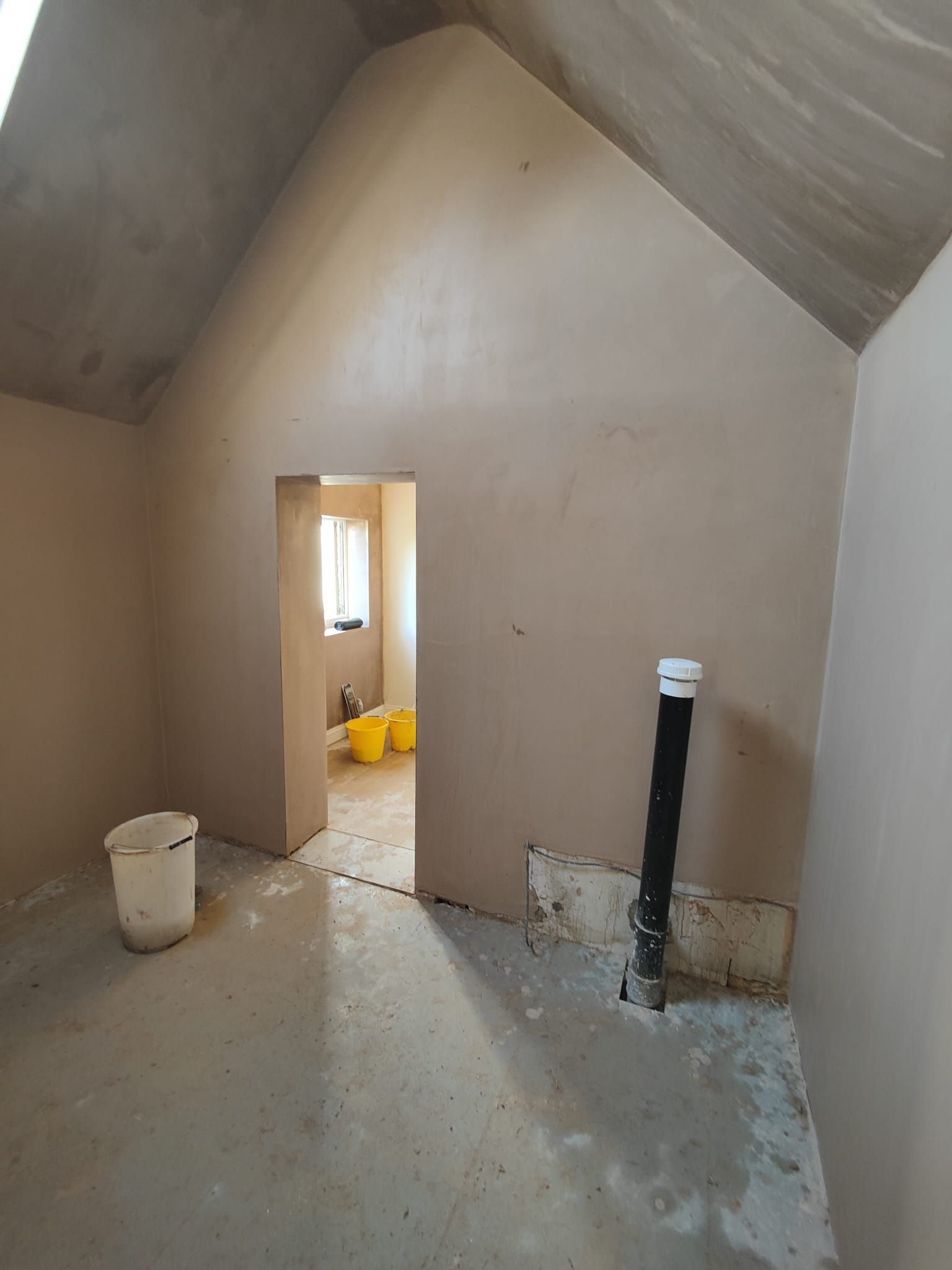 An empty room with a vaulted ceiling and a doorway leading to a bathroom.