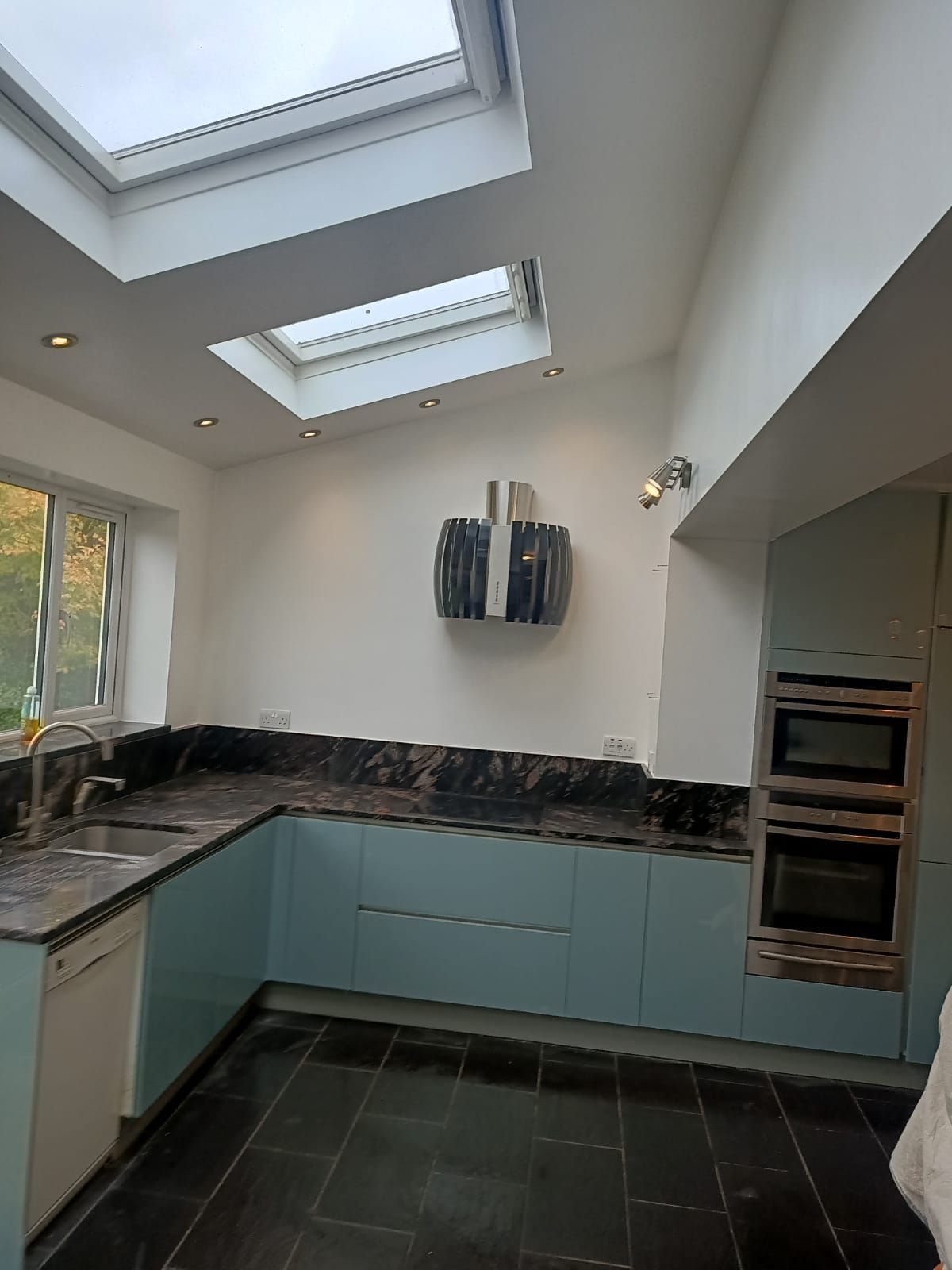 A kitchen with blue cabinets , black counter tops , and a skylight.