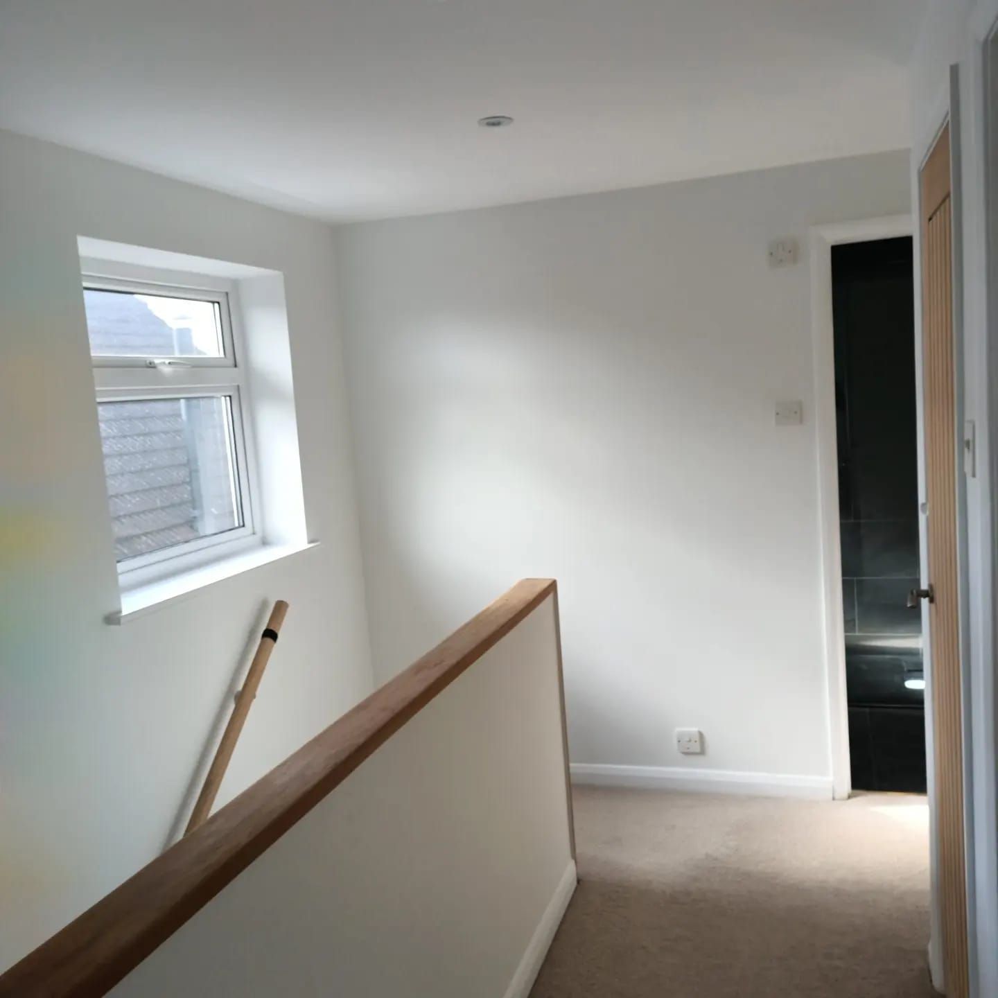 A hallway with white walls and a wooden railing