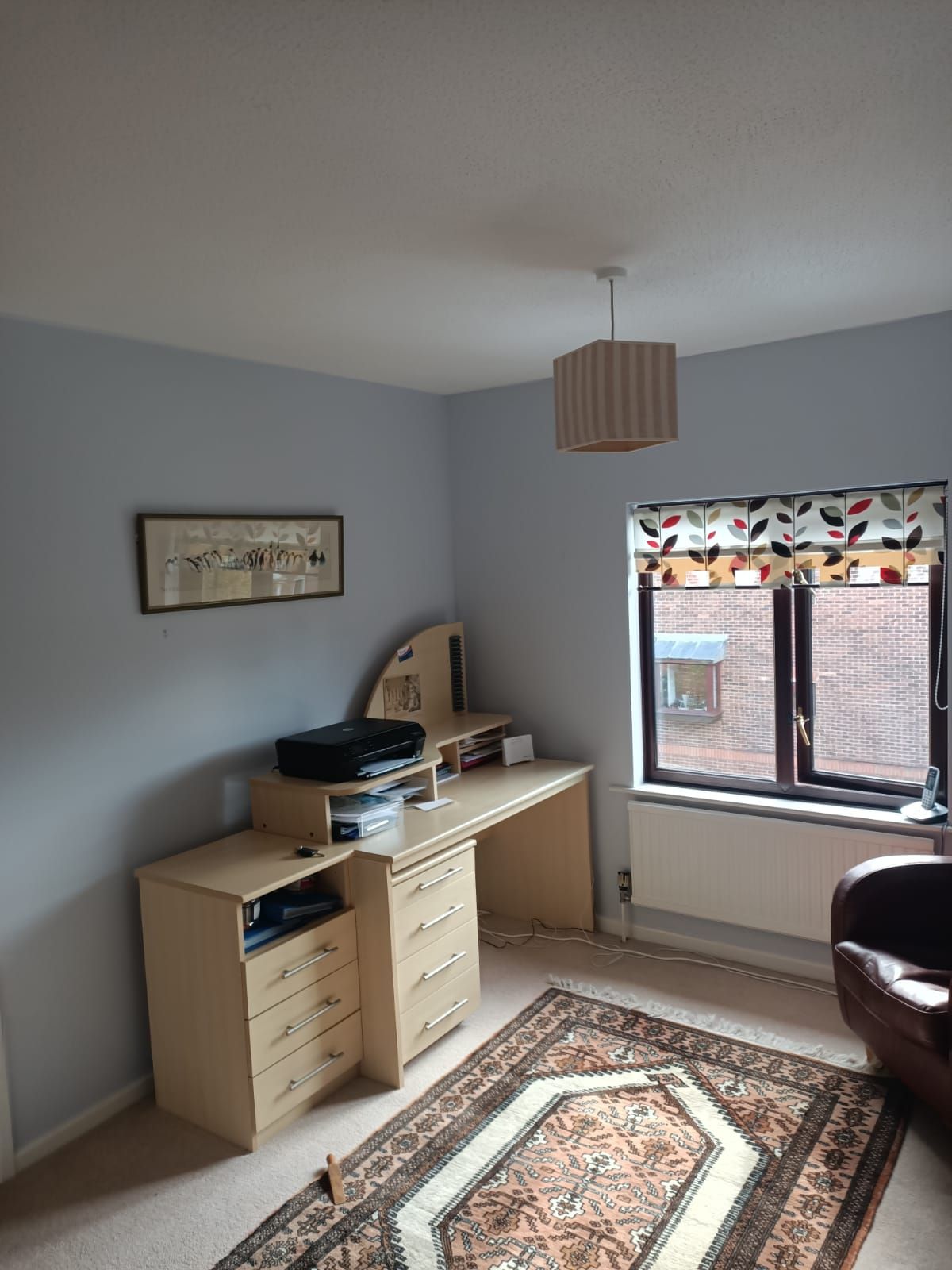 A room with a desk , chair , rug and window.