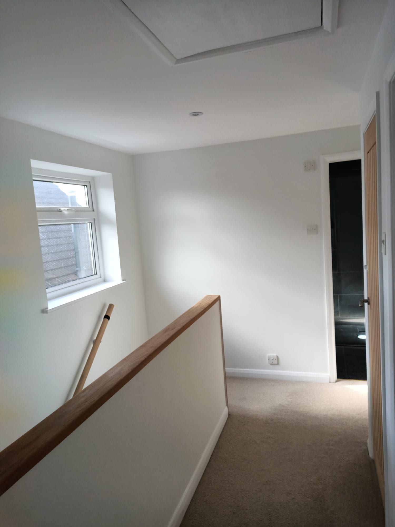 A hallway with white walls and a wooden railing