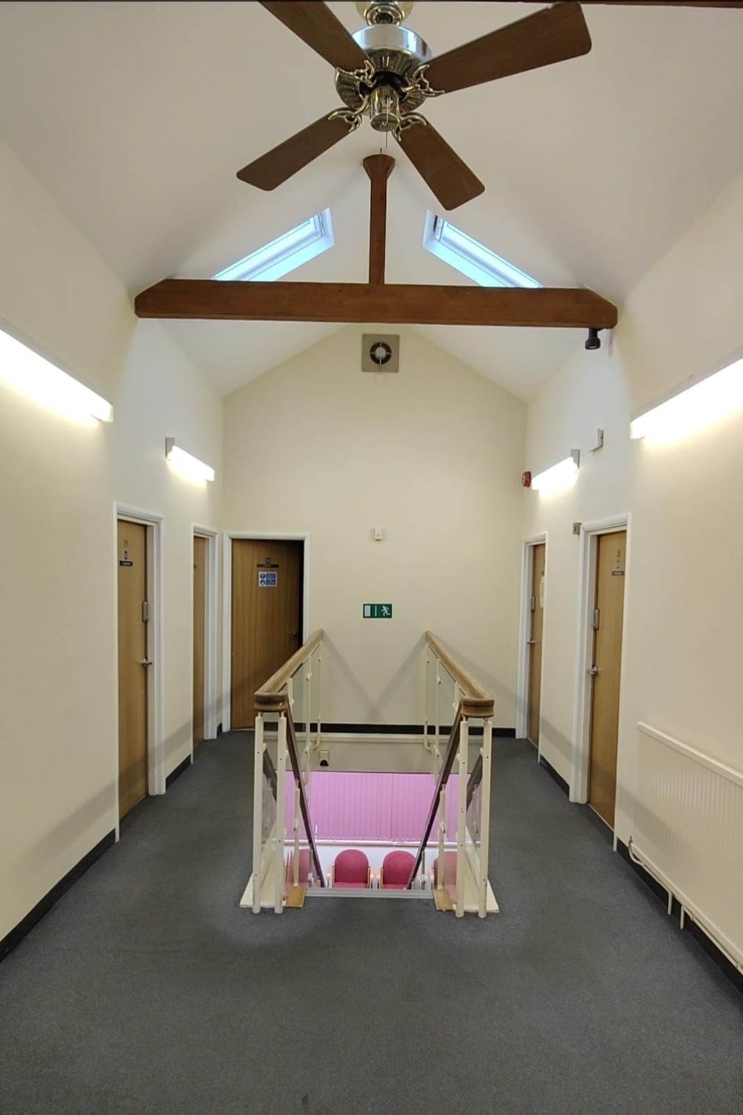 A hallway with a ceiling fan and a green exit sign