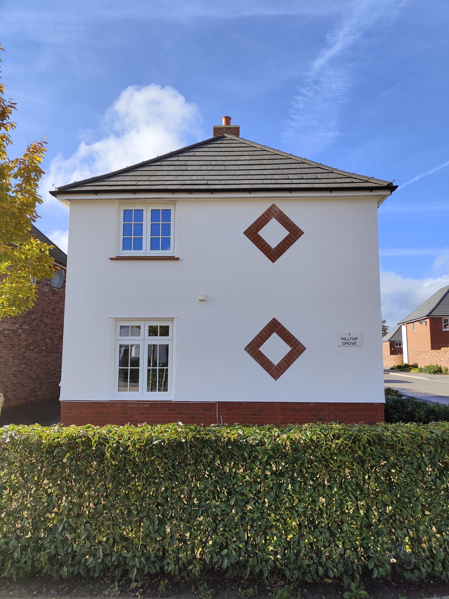 A white house with a roof and a hedge in front of it.