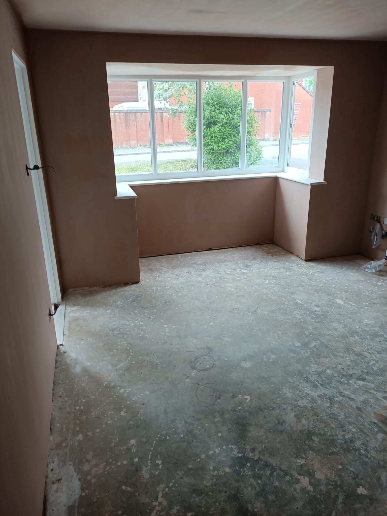 An empty room with a window and a concrete floor.