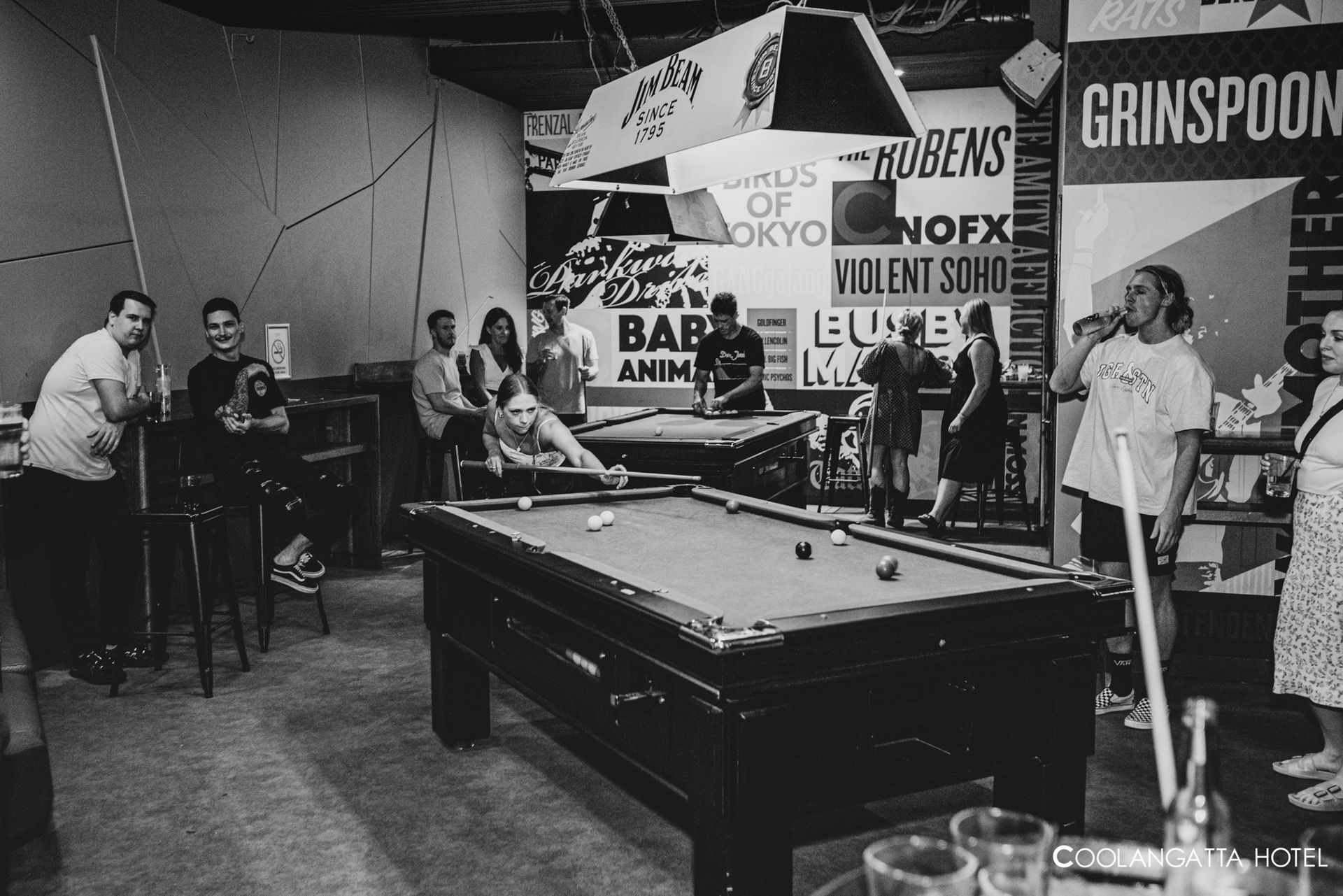 A group of people playing pool in a room with a sign that says grinspoon