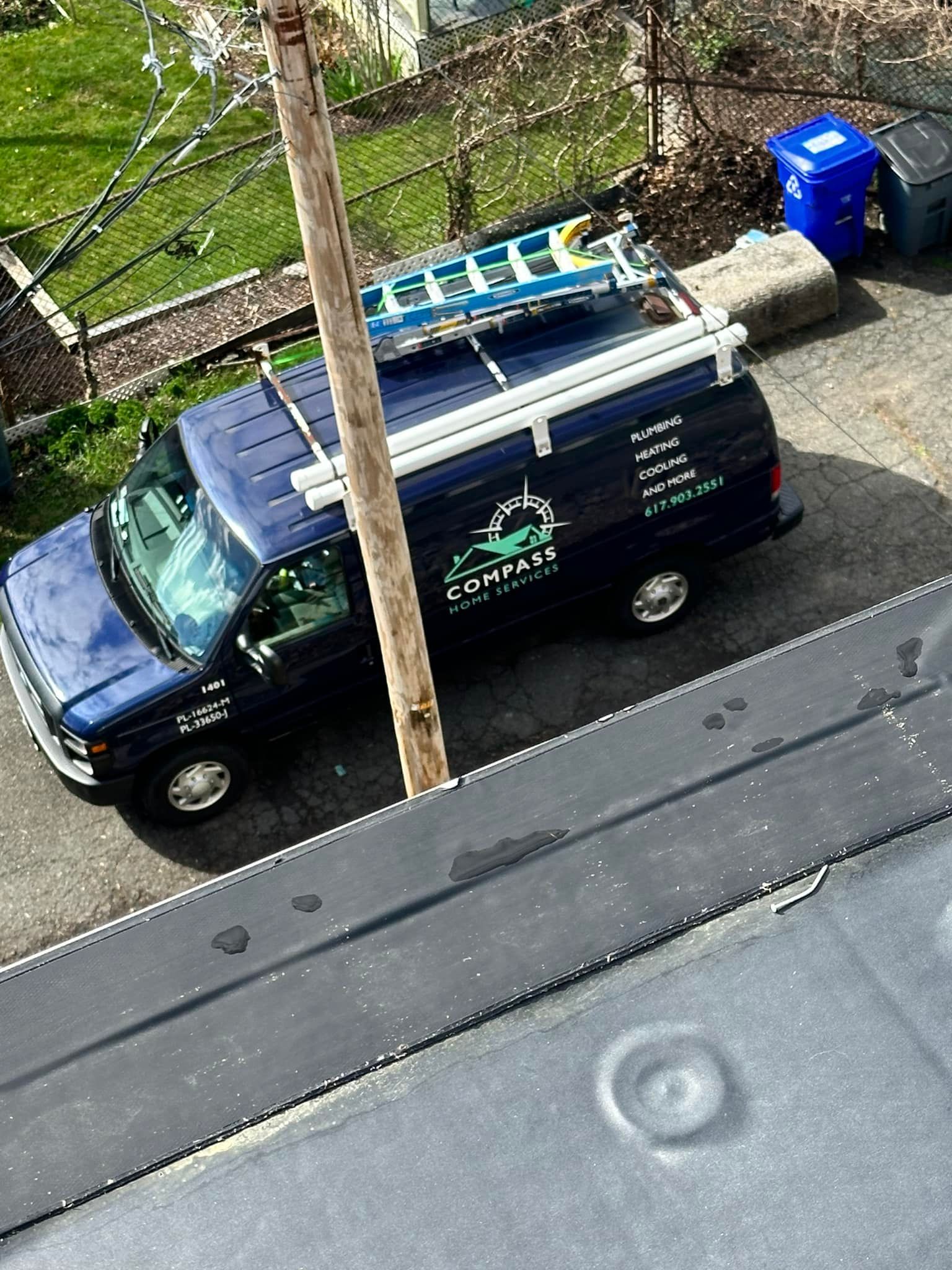 A blue van with a ladder on top of it is parked in a driveway.