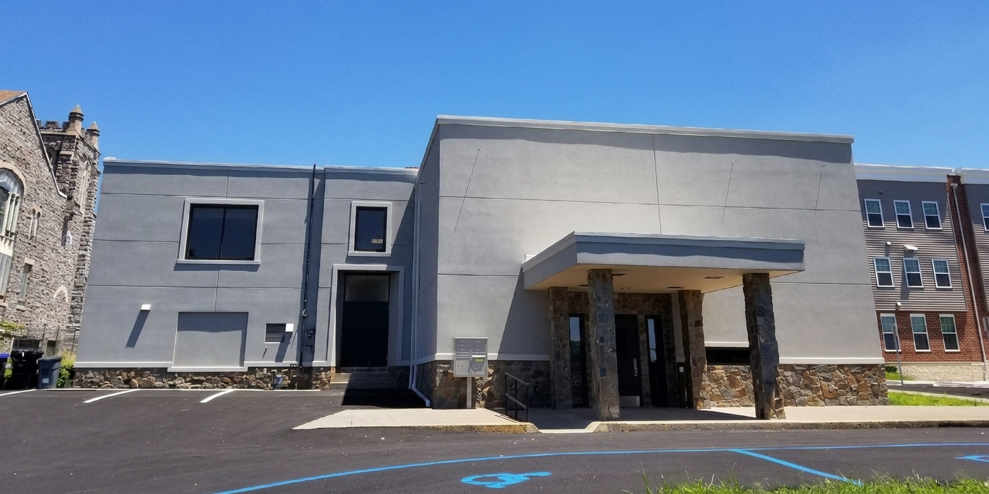 Modern gray building with a covered entrance and parking lot in front