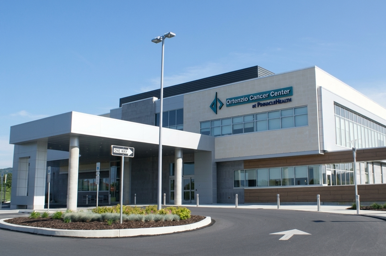 Modern hospital building with blue awning, glass windows, and a parking area in front