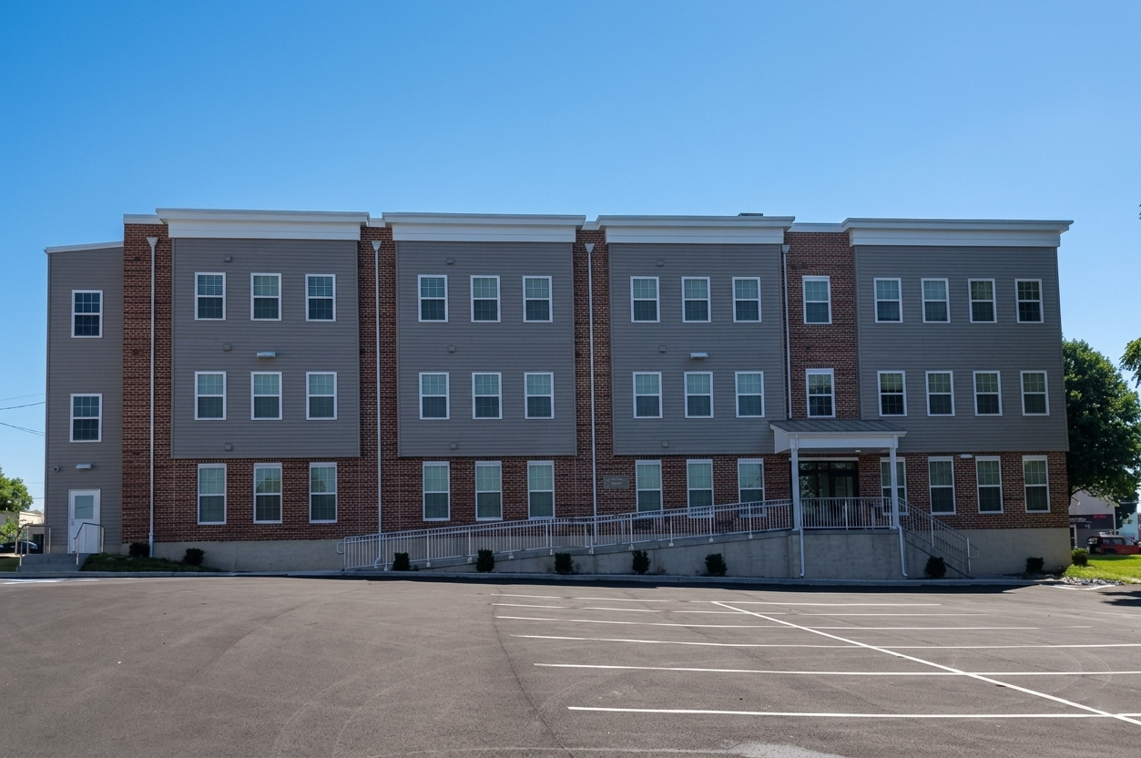 Three-story brick and gray building with a parking lot in front under a clear blue sky