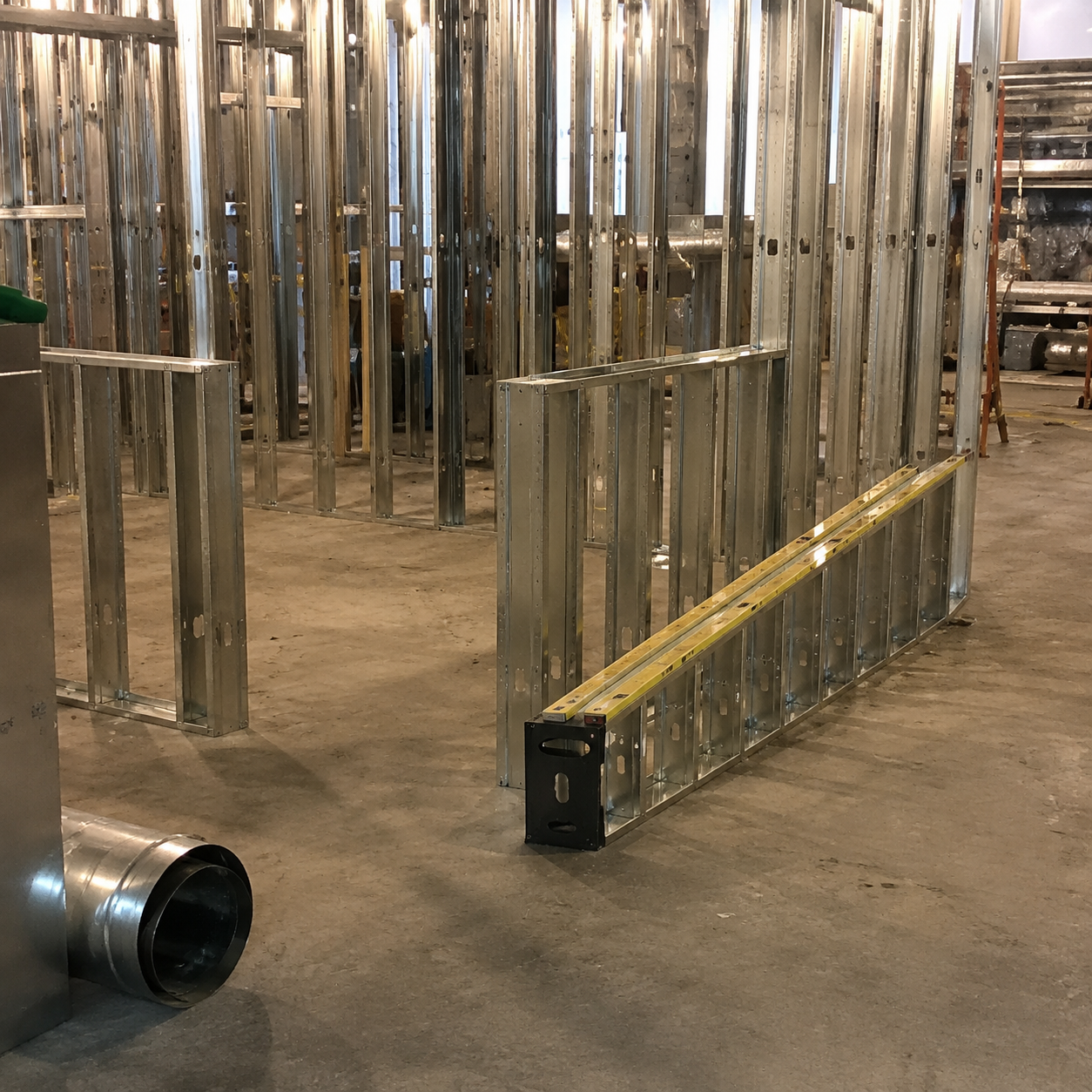 Metal wall framing in an unfinished construction interior, with a yellow measuring tape laid along the floor.