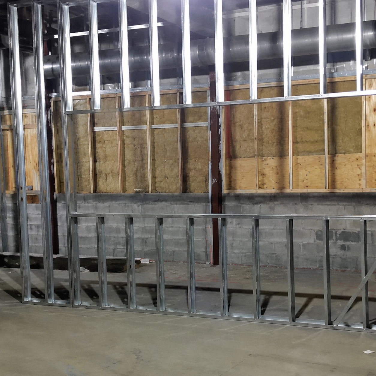 Metal wall framing with insulation panels and exposed concrete floor in a construction site