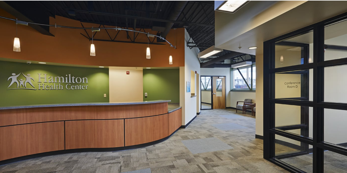 Modern office lobby with curved wood reception desk, green accent wall, and glass entryway
