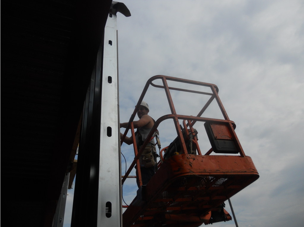 Worker on an orange cherry picker inspecting a tall white structure against a dark background