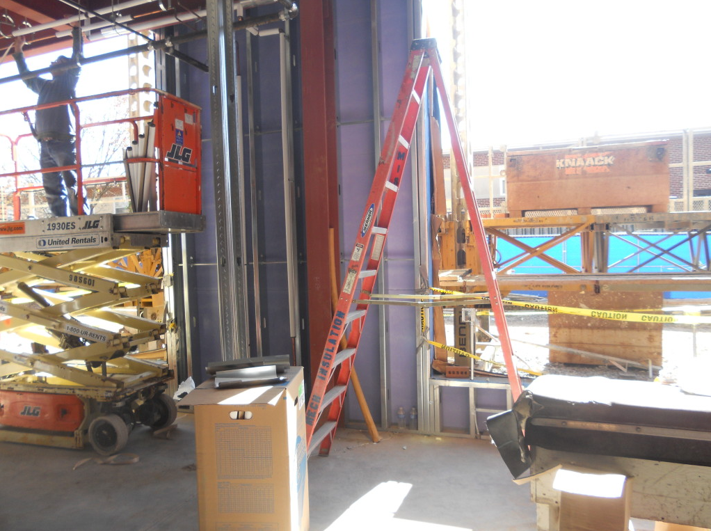 Construction site with ladders, scaffolding, and a glass wall under installation