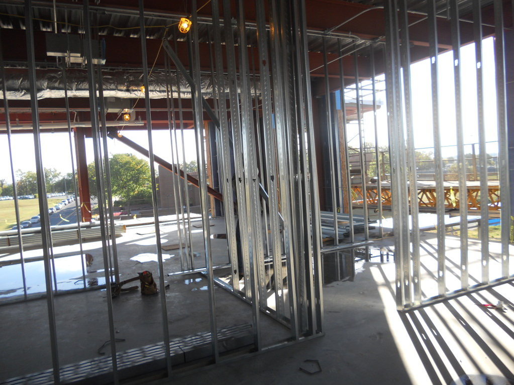 Interior of a building under construction with exposed metal framing and bright daylight streaming through windows.