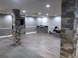 Empty modern room with gray walls, wood-look flooring, stone columns, and a small desk in the back corner