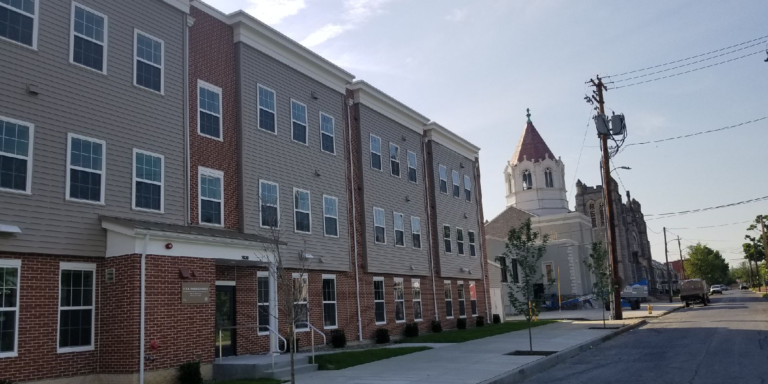 Row of brick-and-gray apartments beside a church tower on a quiet street