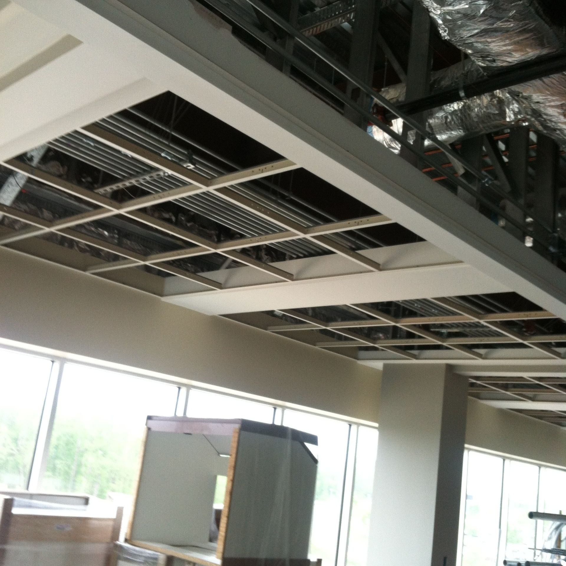 Office interior with exposed ceiling grid, large windows, and a gray cabinet below.